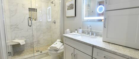 Une salle de bain moderne avec une douche à parois de verre, des toilettes et un meuble-lavabo avec un miroir.