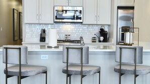 Una cocina moderna con armarios blancos, una isla central con taburetes, iluminación colgante y un refrigerador de acero inoxidable.
