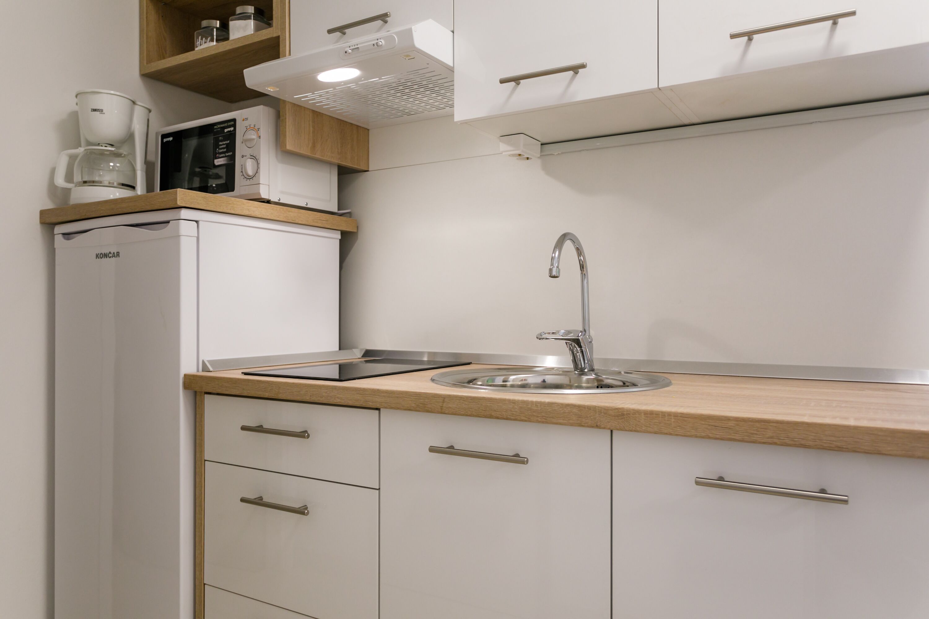 A modern kitchen with white cabinets, a wooden countertop, a built-in microwave, and a stainless steel sink.