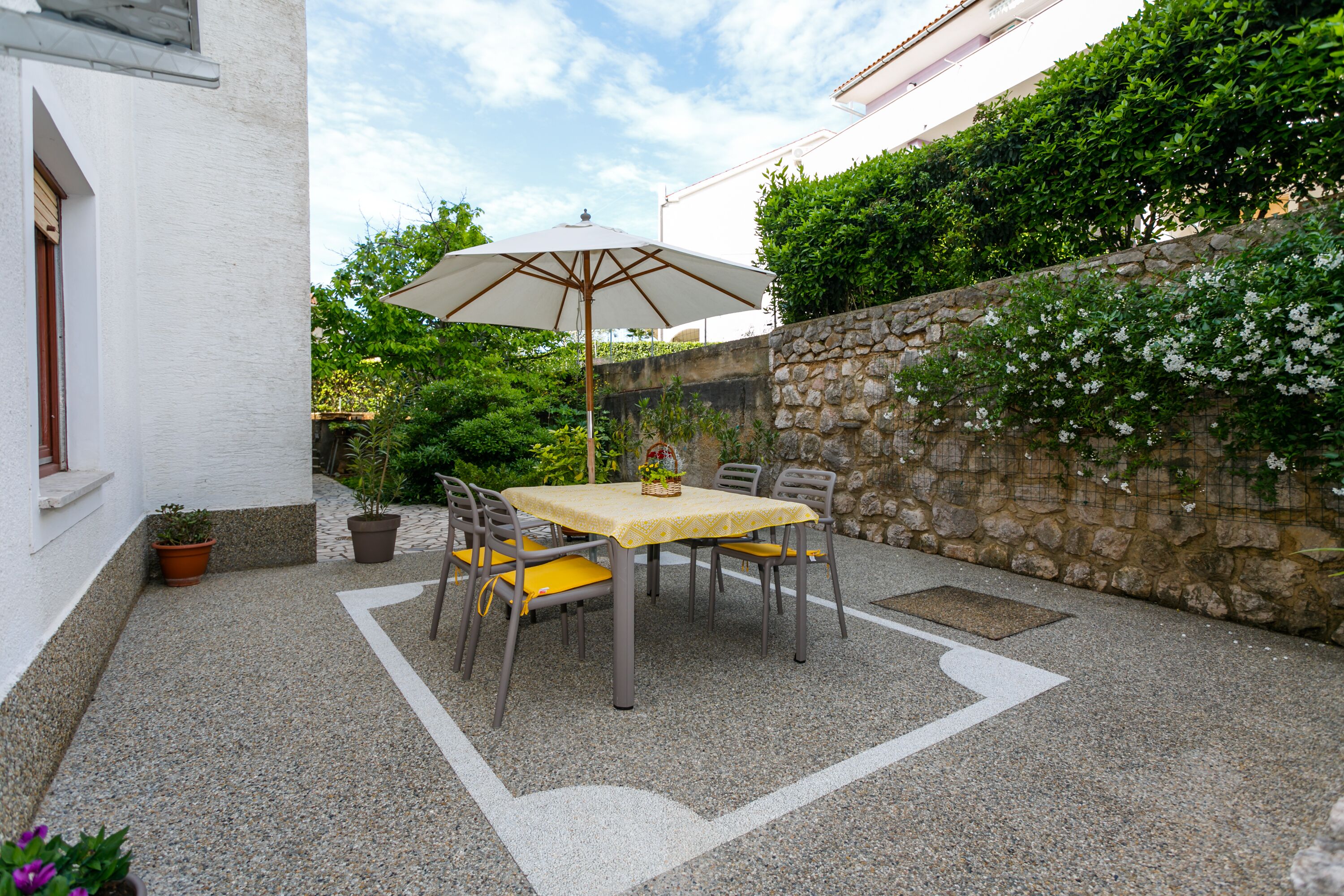 Eine Terrasse im Freien mit Tisch, Stühlen und einem großen Sonnenschirm, sowie einer Steinmauer.