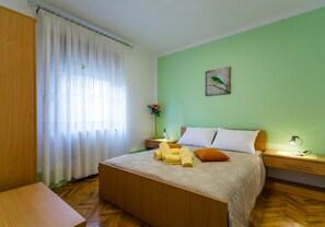 A neatly arranged bedroom with a bed, bedside tables, a nightstand, a lamp, and a painting on the wall.