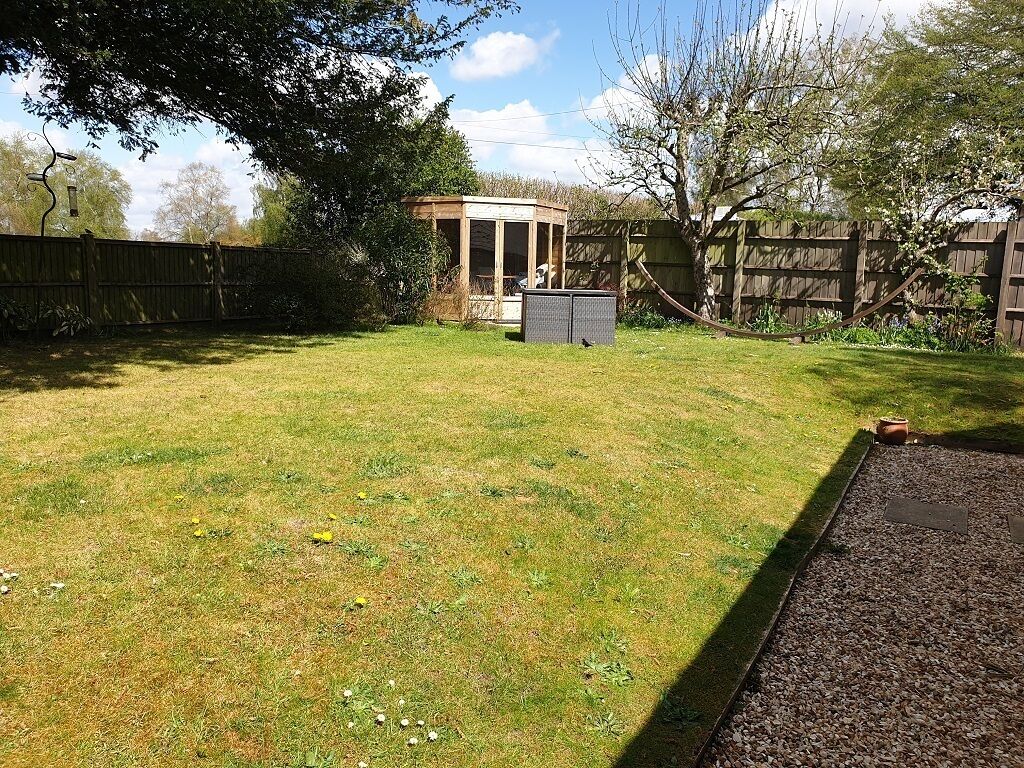 A backyard with a wooden playhouse, a fenced area, and a gravel path.