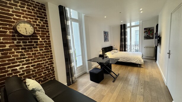 A modern apartment with a brick wall, a black sofa, a dining table, two beds, and large windows. - Gorgeous Paris EIFFEL TOWER (Paris)