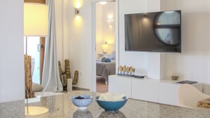 Ein modernes Wohnzimmer mit einem flachbildfernseher an der Wand, einem Sofa, einem Couchtisch mit Dekoration und Blick in den Schlafbereich.