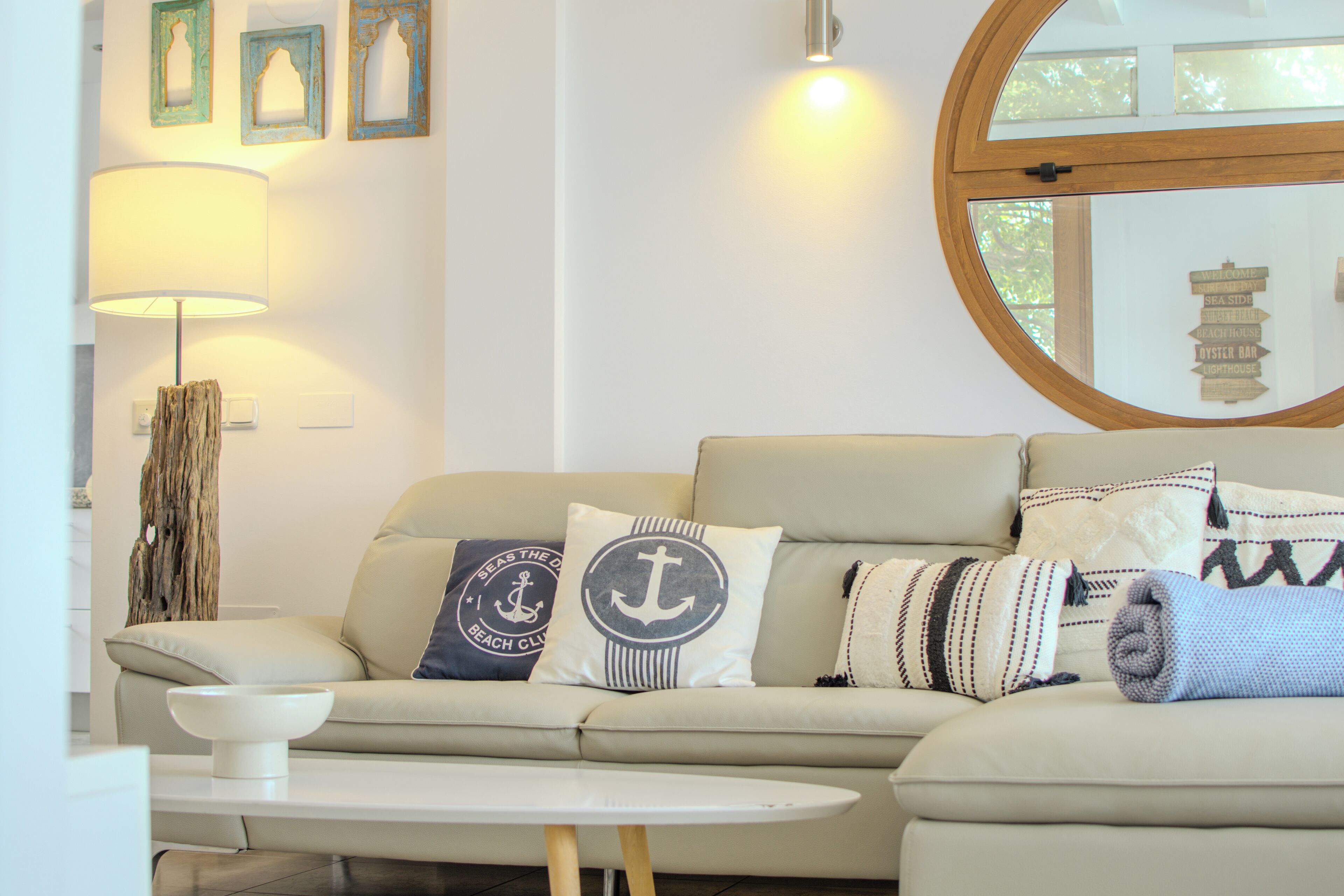 Ein Wohnzimmer mit einem beigen Sofa, einem runden Spiegel und Kissen im maritimen Stil.