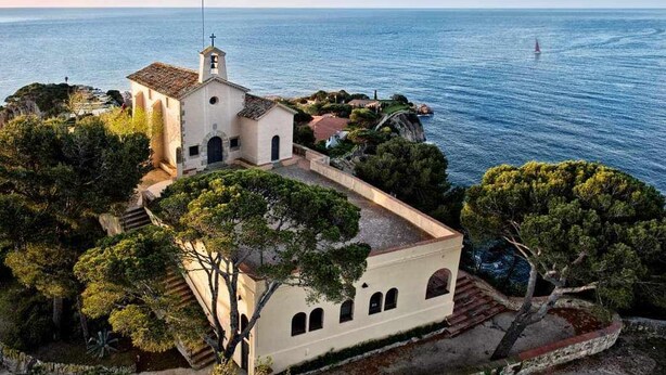 Eine Küstenkirche mit Glockenturm, umgeben von Bäumen und mit Blick auf das Meer.