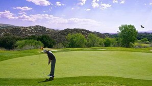 Ein Golfplatz mit einem Golfer, der sich gerade in der Schwungbewegung befindet, umgeben von üppigem Grün und entfernten Bergen.