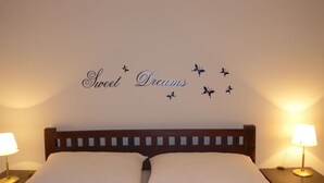 Una cama bien hecha con dos almohadas y una decoración de pared que dice 'Sweet Dreams' con mariposas.