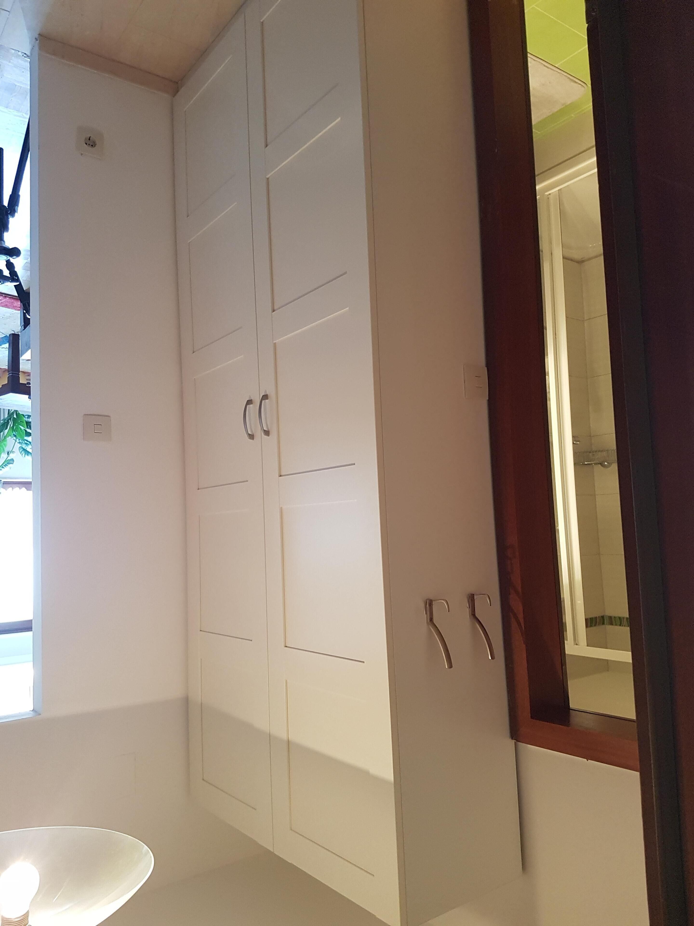 Una habitación con armarios blancos, una pequeña mesa redonda y un espejo con marco de madera.