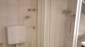 Un baño con inodoro, cabina de ducha y soporte para papel higiénico.