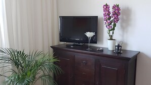 Una sala de estar con un mueble de madera oscura, un televisor de pantalla plana, una planta en maceta y un jarrón decorativo con flores.