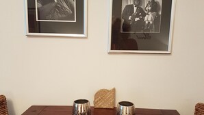 Una mesa de comedor con dos tazas de metal y un plato, con dos fotografías en blanco y negro enmarcadas en la pared.