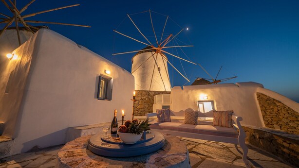 A traditional white-washed building with a windmill, stone walls, and a stone bench. - Unique accommodation in one of the island's iconic windmills (Mikonos)