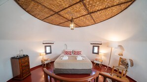 A bedroom with a large bed, two bedside tables, a wooden dresser, a hanging light fixture, and a wooden chair. - Unique accommodation in one of the island's iconic windmills (Mikonos)