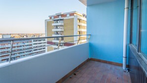 Uma varanda com piso de azulejos, guarda-corpo de metal e vista para um edifício de vários andares.