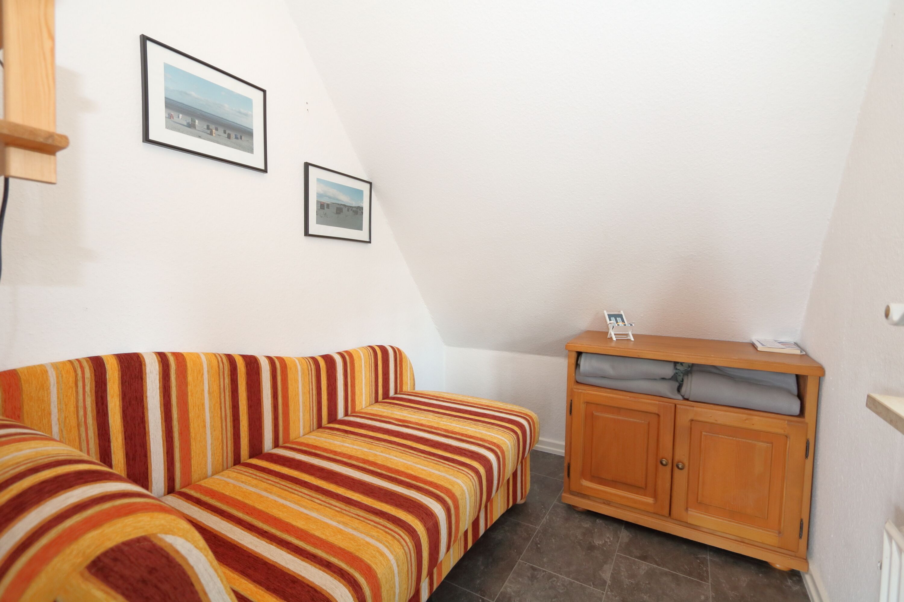 A corner room with a striped sofa, a wooden cabinet, and two framed pictures on the wall.