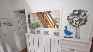 Un couloir avec une console blanche, un miroir, une plante en pot et un arrangement floral.