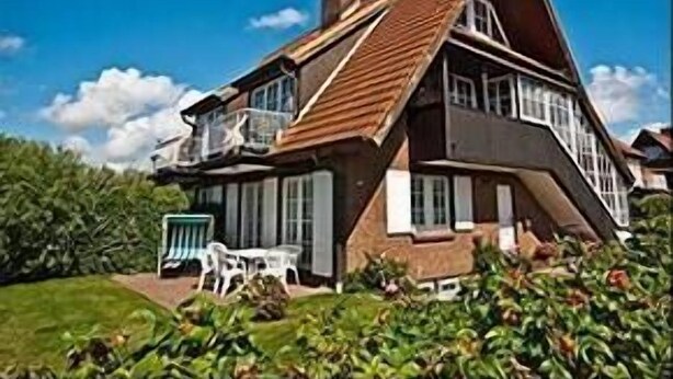 Une grande maison à deux étages, dotée d’un toit à forte pente et de nombreuses fenêtres.
