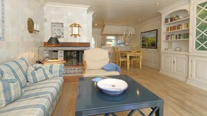 A living room with a sofa, a coffee table, a fireplace, a dining area, and a kitchen with white cabinets and a bookshelf. - Welcome to Haus Ruusenhoog, the versatile vacation home located in picturesque Braderup (Braderup)