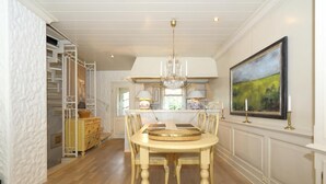 A dining area with a round table, chairs, and a chandelier. There is a kitchen in the background with cabinets and a painting on the wall. - Welcome to Haus Ruusenhoog, the versatile vacation home located in picturesque Braderup (Braderup)