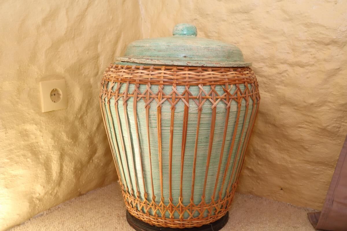A woven basket with a lid, placed against a textured wall with a power outlet nearby.