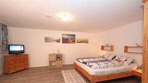 A bedroom with a wooden bed, a dresser, a television, and wall-mounted shelves. - South beach 11 (Westerland)