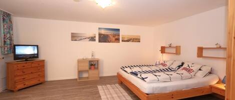A bedroom with a wooden bed, a dresser, a television, and wall-mounted shelves.