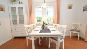 A dining area with a white table set for four, a cabinet with glass doors, and a window with curtains. - South beach 11 (Westerland)