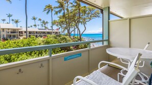 Ein Balkon mit Blick auf den Strand, Palmen und ein Gebäude im Hintergrund.