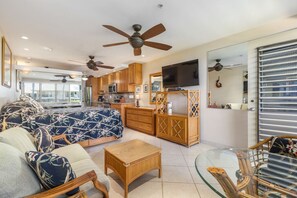 A spacious living area with a large bed, wooden furniture, ceiling fans, and a television.