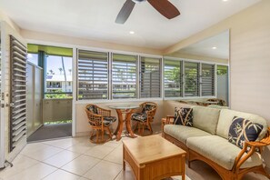 A spacious room with a large window, a ceiling fan, a sofa, and a dining table with chairs.