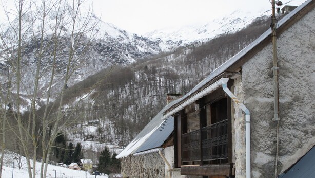 A stone building with a wooden door and a metal balcony, set against a snowy mountain backdrop. - Welcome to Hautes-Pyrénées (Campan)