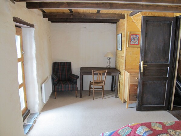 A room with a wooden desk, two chairs, a lamp, and a door.