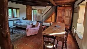 A rustic interior with a wooden dining table, a checkered sofa, and a staircase leading to an upper level. - Welcome to Hautes-Pyrénées (Campan)