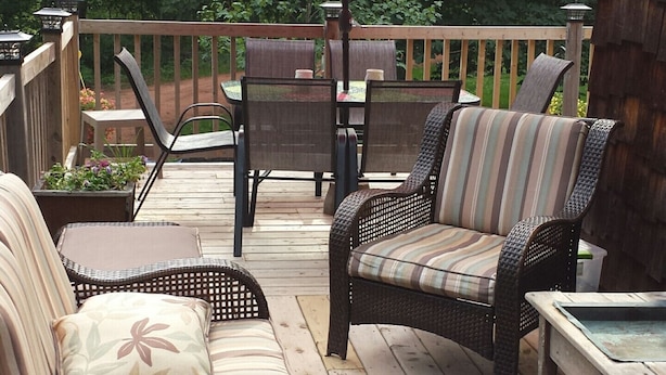 A wooden deck with wicker furniture, including two chairs and a table, under a red umbrella. - Chestnut Lane Bed & Breakfast - The Blue Room (New Glasgow)