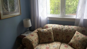 A corner sofa with floral upholstery, a side table with a lamp, and a framed picture on the wall. - Chestnut Lane Bed & Breakfast - The Blue Room (New Glasgow)