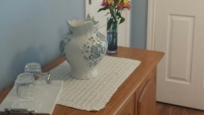 A wooden dresser with a vase of flowers, a framed picture, and a glass on a table. - Chestnut Lane Bed & Breakfast - The Blue Room (New Glasgow)
