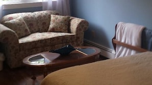 A bedroom with a bed, a chair, a small table, a ceiling fan, and a window with curtains. - Chestnut Lane Bed & Breakfast - The Blue Room (New Glasgow)