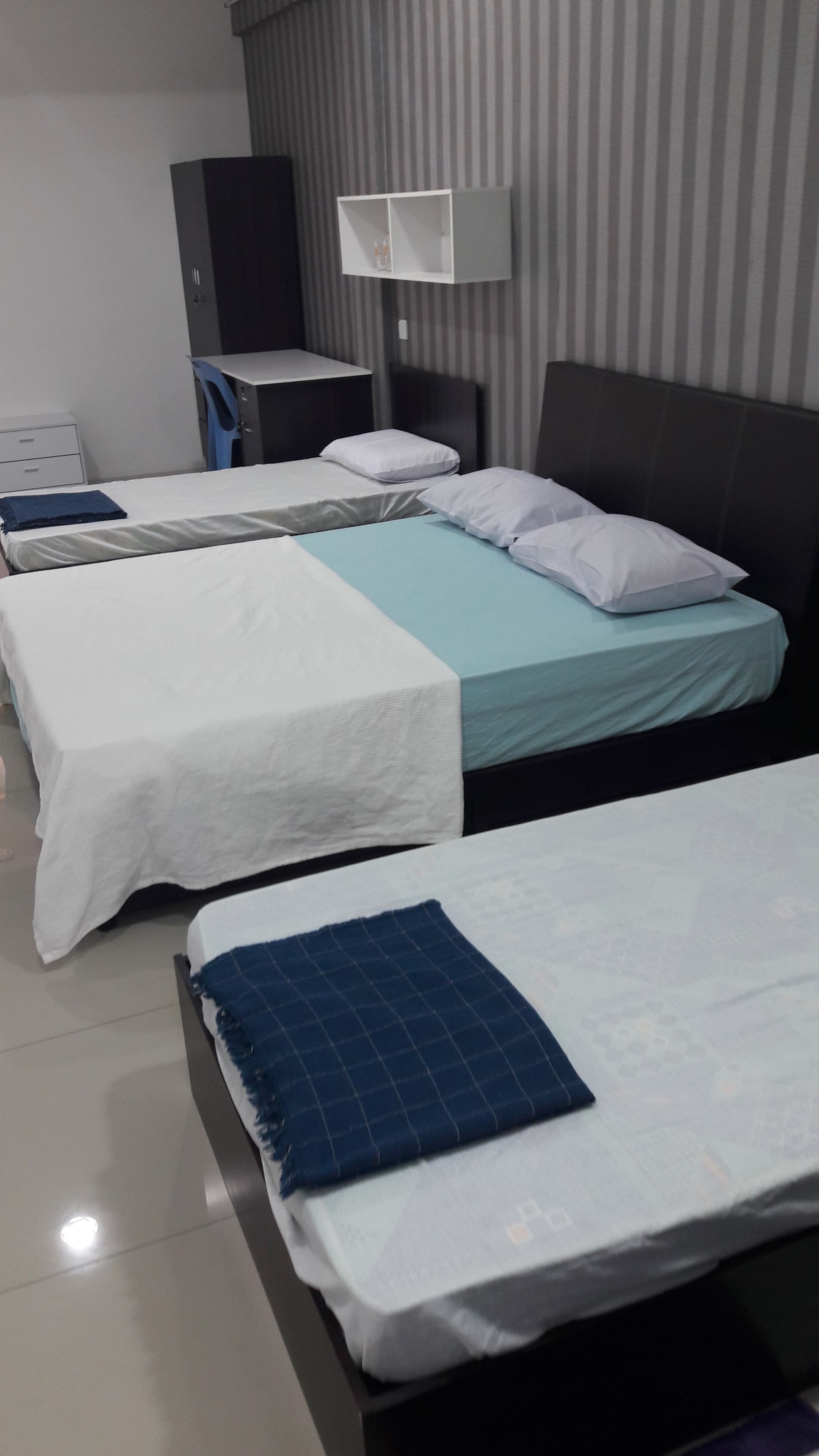 A hotel room with three beds, a desk, a chair, and a lamp.