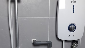 Un système de commande de douche DEKA fixé sur un mur carrelé, équipé d’un pommeau de douche à main et de tuyaux flexibles.
