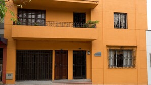 A two-story building with a balcony on the upper floor, a gated entrance, and a small window with decorative bars. - Casa Hotel Alnor-Med (Medellín)