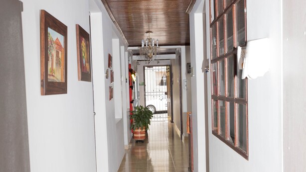 A hallway with a wooden ceiling, tiled floor, and framed pictures on the walls. - Casa Hotel Alnor-Med (Medellín)