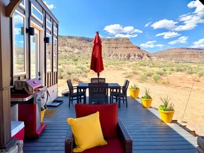 Una terrazza con un divano rosso, un tavolo e sedie, affacciata su un paesaggio desertico con montagne.