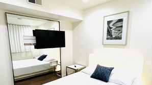 A hotel room with a bed, a bedside table, a mirror, a TV, and a framed picture on the wall. - 3BR Condo SALE nexttoSTRIP nearLVCC sale modern stylish WiFi pool Labor Day Sema (Las Vegas)