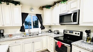 A kitchen with white cabinets, a stainless steel stove, a microwave, and a window with curtains. - 3BR Condo SALE nexttoSTRIP nearLVCC sale modern stylish WiFi pool Labor Day Sema (Las Vegas)