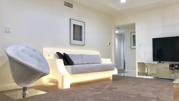 A modern living room with a white sofa, a glass coffee table, a flat-screen TV, and a unique chair. - 3BR Condo SALE nexttoSTRIP nearLVCC sale modern stylish WiFi pool Labor Day Sema (Las Vegas)