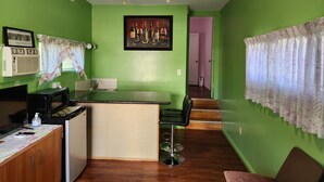 Una cocina con pared verde, barra, microondas, refrigerador y fregadero.