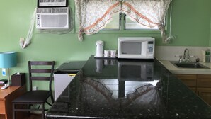 Una cocina con microondas, lavamanos y ventana con cortinas florales.