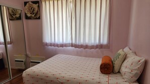 Un dormitorio con cama, almohadas, una ventana con cortinas, un espejo y un adorno en la pared.