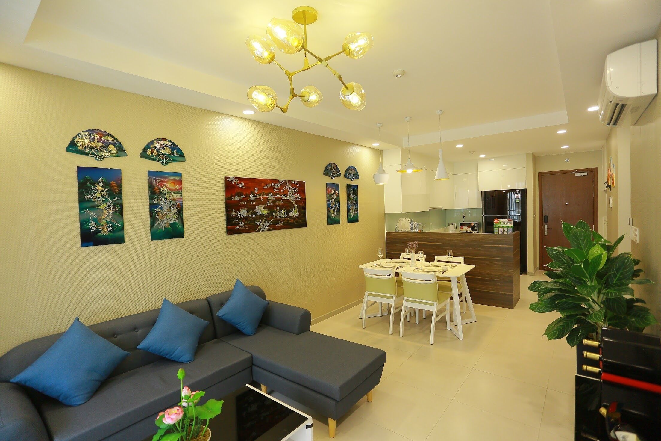 A modern living room with a grey sectional sofa, a dining area with a white table and chairs, and a kitchen in the background.